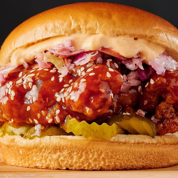Close-up of a Hot Chicks fried chicken sandwich with sauce, coleslaw, and pickles on a bun.