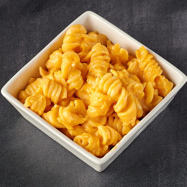 A white square bowl filled with creamy, orange macaroni and cheese on a dark background.