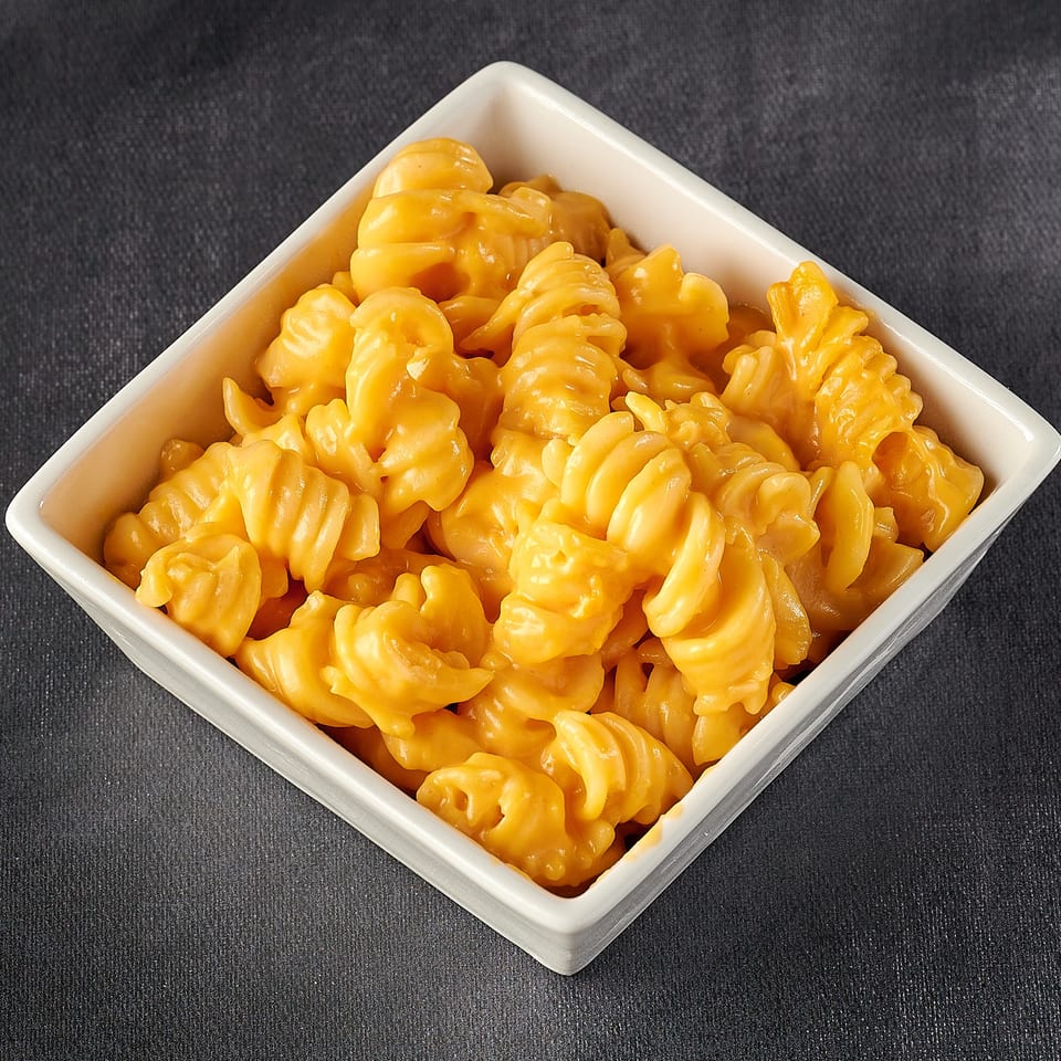 A white square bowl filled with creamy, orange macaroni and cheese on a dark background.