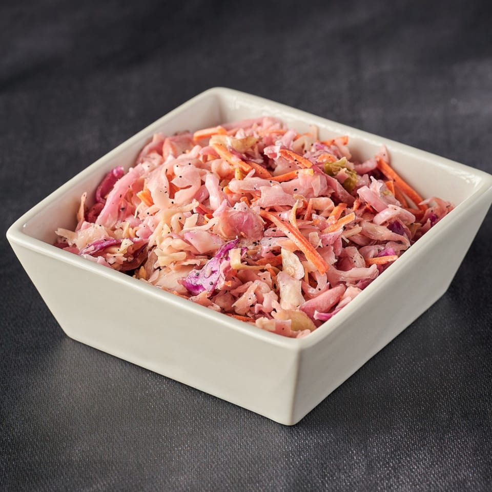 A white square bowl filled with Hot Chicks House of Chicken coleslaw, featuring shredded cabbage and carrots.