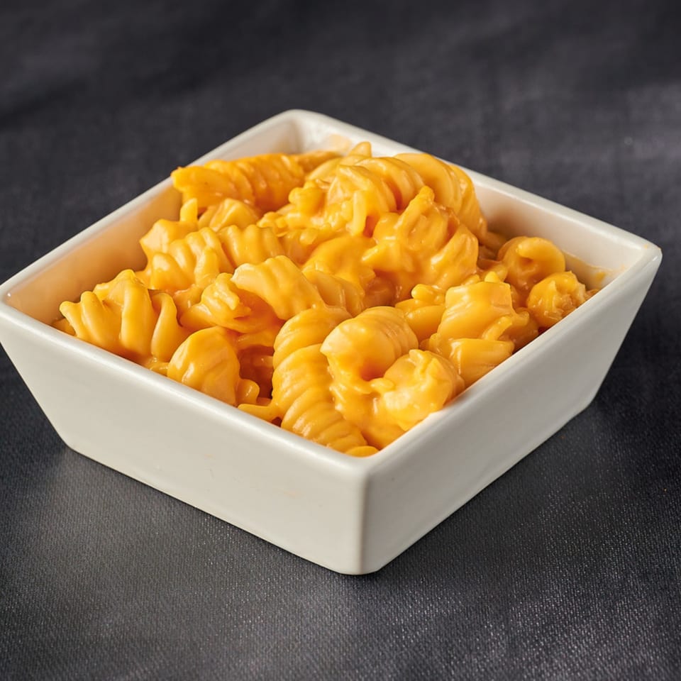 A white square bowl filled with creamy orange macaroni and cheese on a dark background.