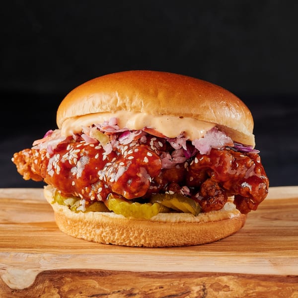 Hot Chicks House of Chicken sandwich with crispy fried chicken, red sauce, sesame seeds, and pickles.