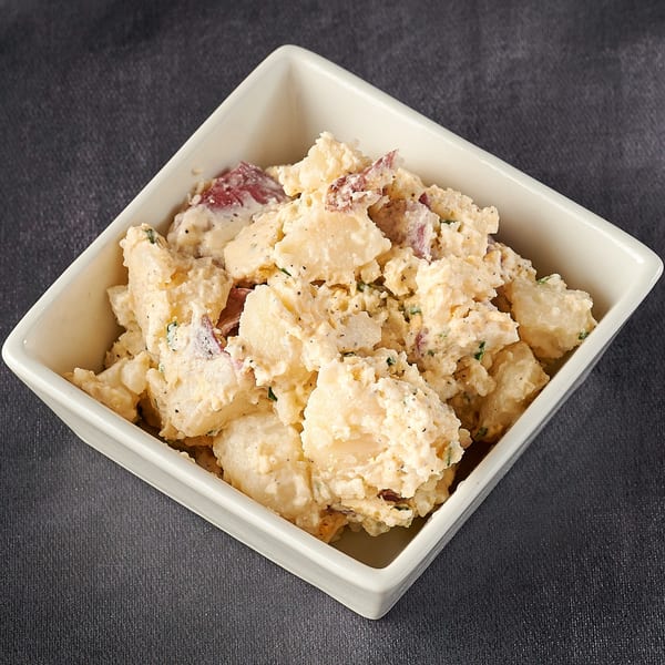 Creamy potato salad with red potato skins and herbs in a white square bowl.