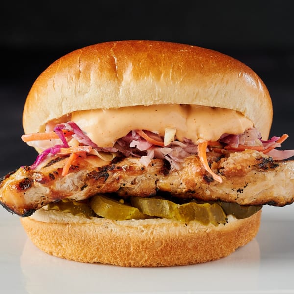 Hot Chicks House of Chicken sandwich with grilled chicken, coleslaw, sauce, and pickles on a bun.